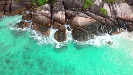 Drone-shot-of-waves-crashing-on-large-granite-stone-at-baie-lazare,-Mahe-Seychelles-60-fps
