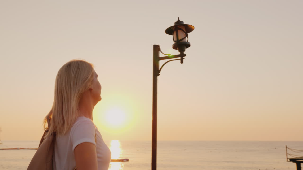 una donna felice cammina allegramente lungo il molo in riva al mare con un cappello in mano ammirando il