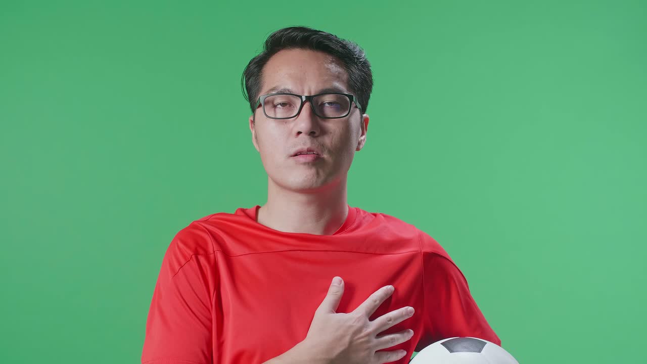 녹색 스크린 배경에서 축구 선수를 응원하면서 공을 들고 국악을 부르는 아시아 남자의 클로즈업