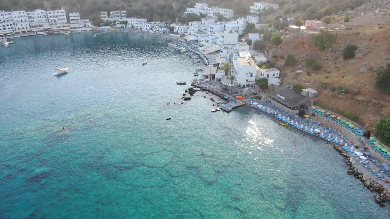 vista de drones en grecia volando sobre el mar azul claro en loutro pequeña ciudad de casas blancas y pequeños barcos al lado de una colina en un día soleado