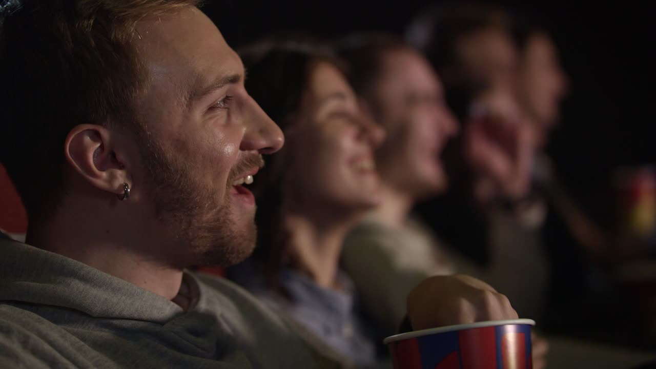 Young guy with earring in his ear eating popcorn laughing when watching movie