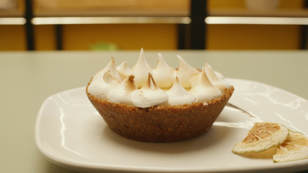 Close-up of an exquisite lemon tart with toasted meringue served on a white plate. Handmade dessert with a golden texture and creamy finish