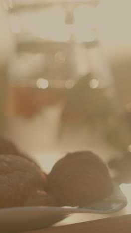 primer plano de la configuración de picnic en una mesa de madera con croissants frescos, uvas verdes, rebanadas de naranja y melocotón bajo la luz del sol dorada, jarro de agua refrescante en el fondo, con fondo borroso