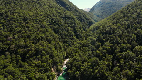 aerial drone shot over blue pools river water flowing through green vegetation covered mountain range in new zealand