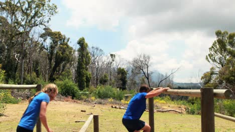 fit man and woman climb a hurdles during obstacle course