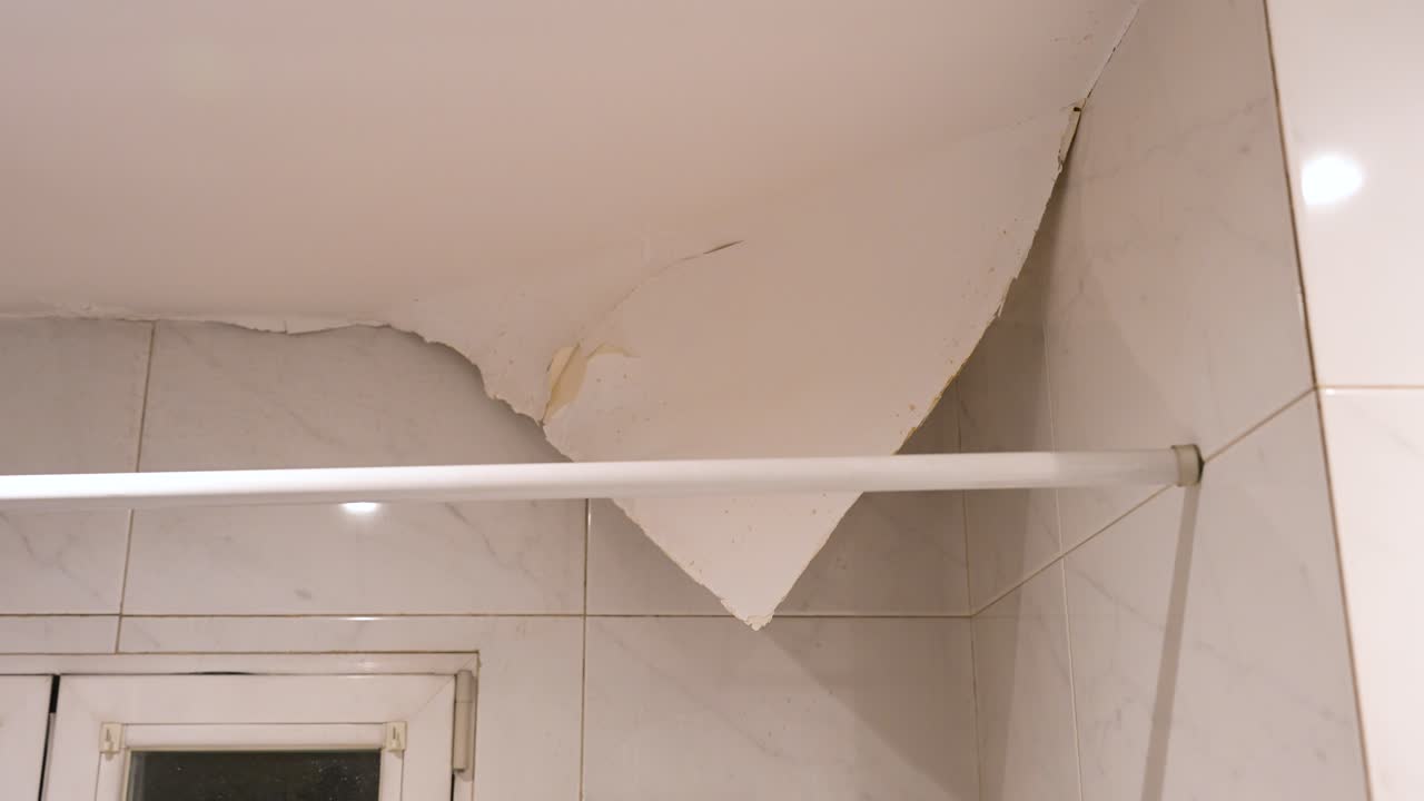 Grave danno causato dall'acqua in un bagno: la pittura si stacca dal soffitto a causa dell'elevata umidità e dell'infiltrazione di acqua. Concept di ristrutturazione e richiesta di risarcimento assicurativo