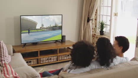 composite of happy family sitting at home together watching javelin athletics event on tv