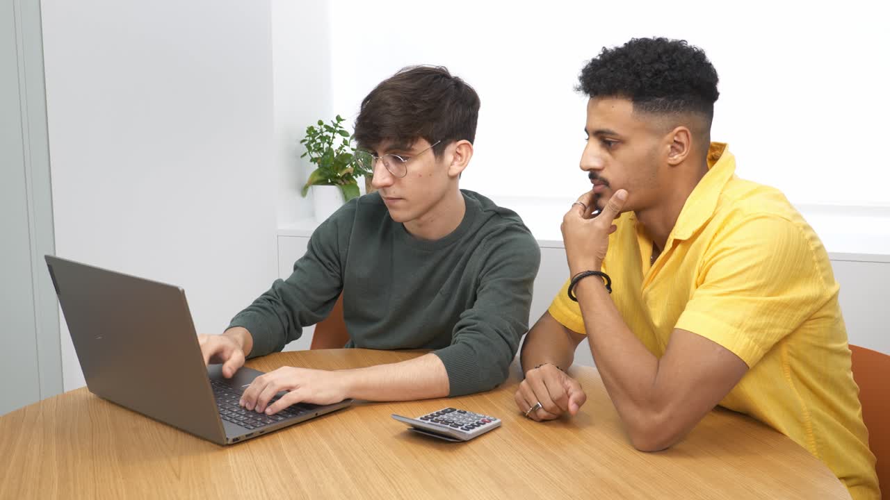 Two young businessmen collaborating on a laptop at a modern office