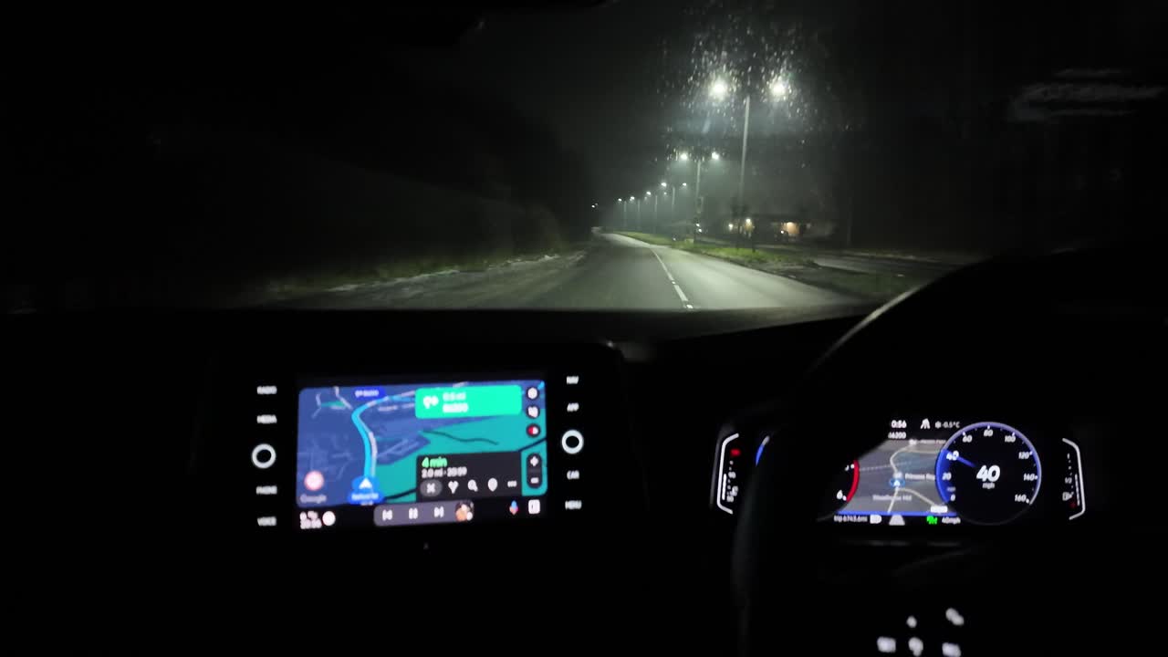 Night driving view showing car navigation display, dashboard, and dimly lit road.