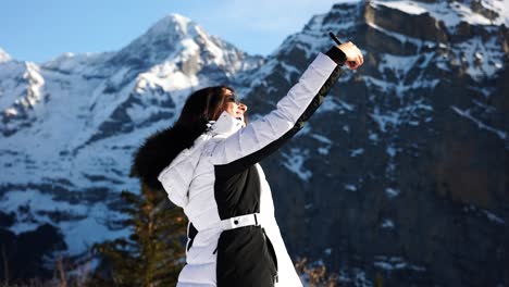 young brunette female hold phone and take selfies with switzerland mountains