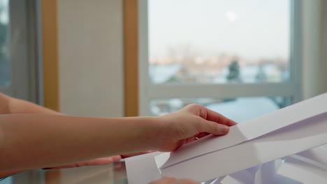 hand view of kids folding white plain paper at table, background showing blurred window with snow outside, focus on hands and paper, creating a quiet and cozy crafting environment