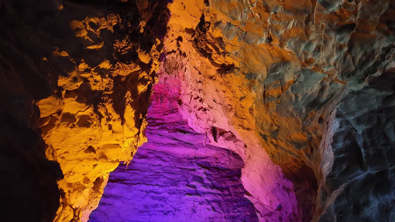 Interior deslumbrante de uma caverna de calcário em Zhangjiajie, com iluminação artificial vibrante roxa e laranja em estalactites e paredes rochosas
