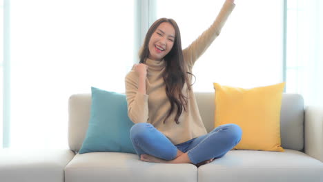 a young woman sitting on a couch energetically expresses her feelings of success while holding a fan on one hundred dollar bills