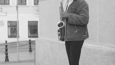 black and white view of a sax case with coins on the floor and a man in jacket playing sax in the street