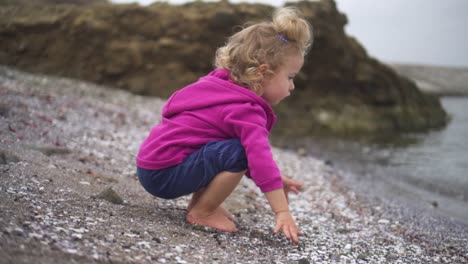 a cute girl in purple hoodie playing pebbles on the beach - medium shot, slow motion