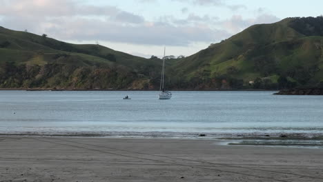 Dos-Personas-Remando-En-Licitación-Para-Llegar-A-Un-Velero-En-La-Bahía,-Nueva-Zelanda