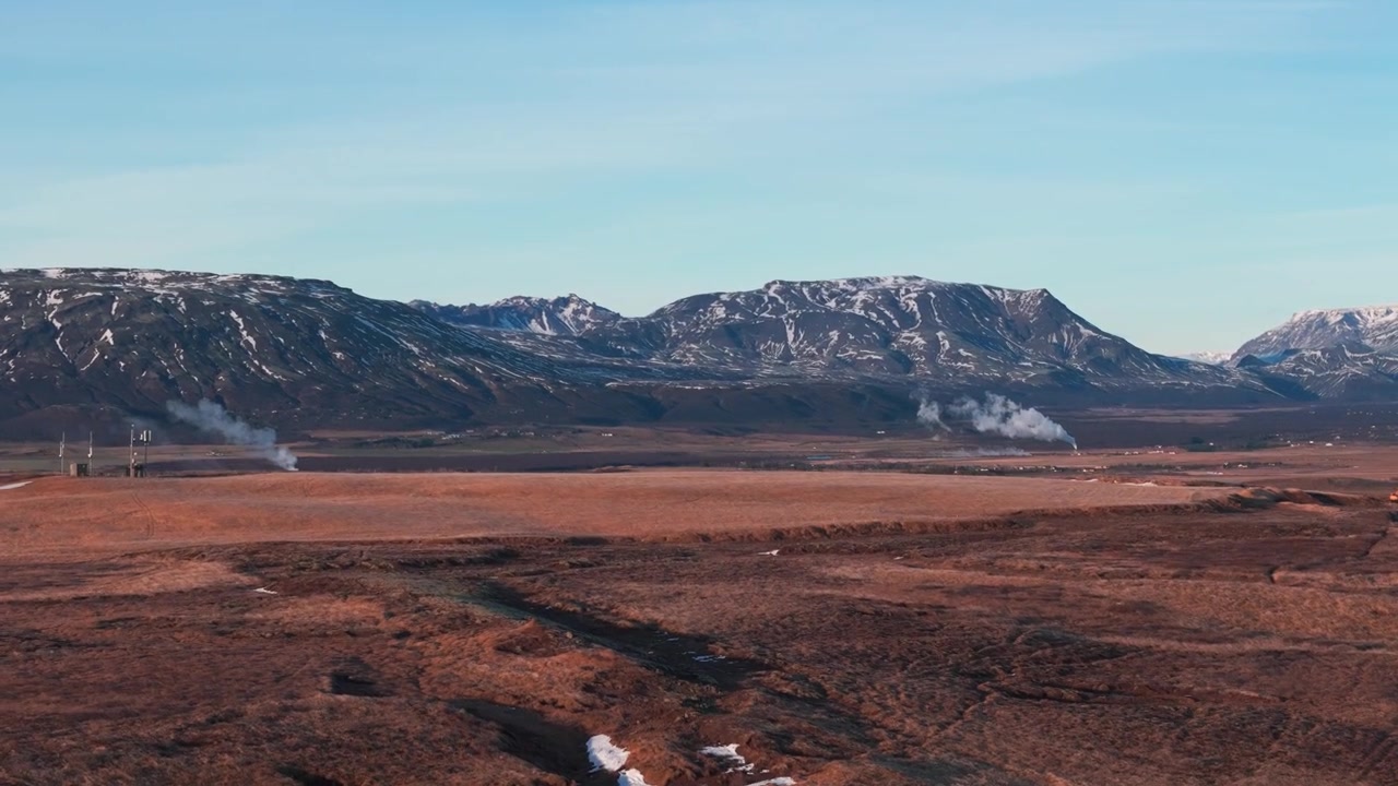 Geotermisk kraftverk med fantastiske snødekte fjell i bakgrunnen.