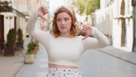 Upset-redhead-woman-showing-thumbs-down-sign-disapproval-dissatisfied-bad-work-mistake-in-city