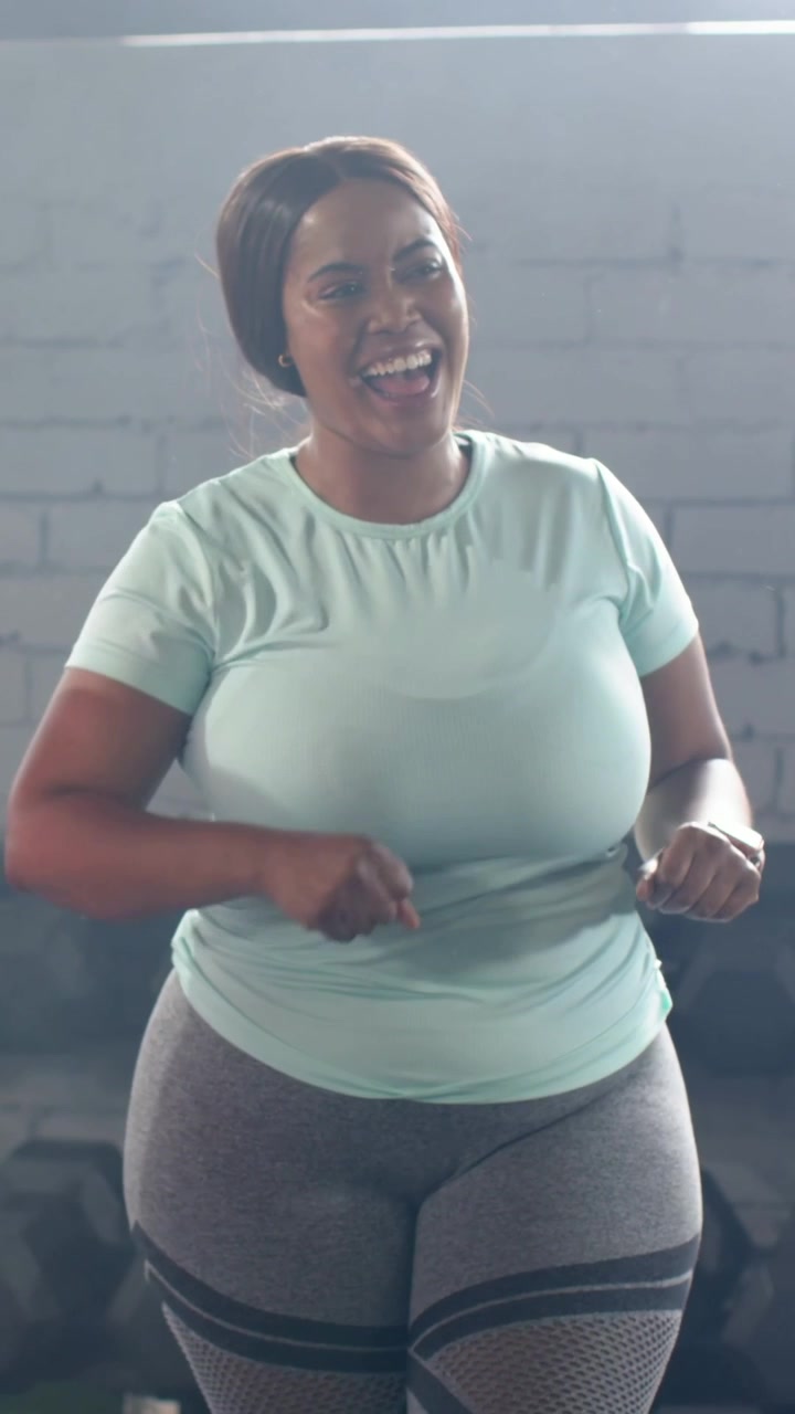 Video verticale: Donna con maglia verde acqua che fa un cenno, muovendo le braccia e mimando il gesto di girare dei rubinetti in palestra con manubri e orologio.