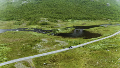 Coche-Conduciendo-Por-El-Largo-Y-Sinuoso-Camino-A-Lo-Largo-Del-Exuberante-Campo-Y-El-Tranquilo-Lago-En-Hydalen,-Una-Joya-Escondida-En-Hemsedal,-Noruega-En-Una-Mañana-Brumosa---Drone-Aéreo