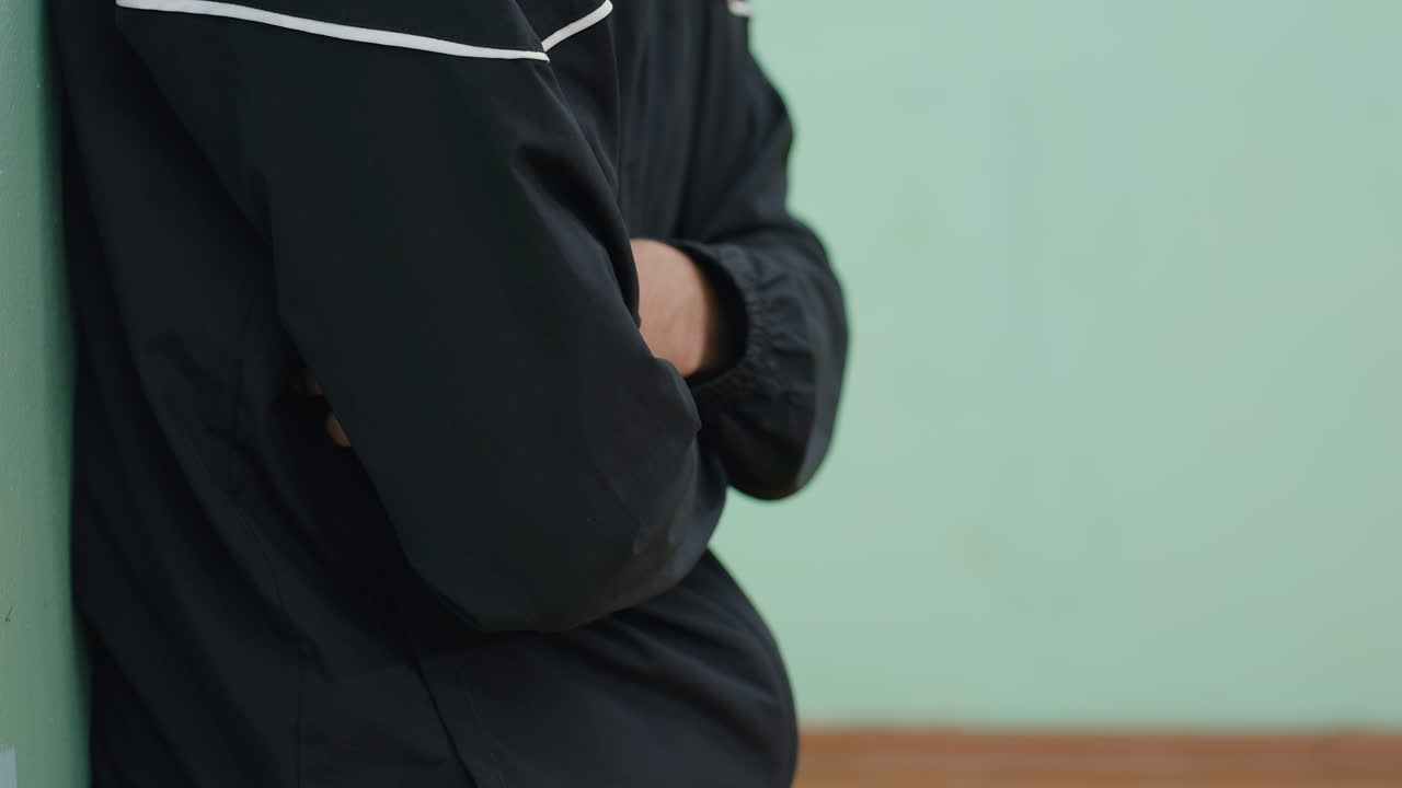 Close up of person in black jacket leaning against wall with arms folded, relaxed stance showing calm posture and still moment, highlighting casual lifestyle