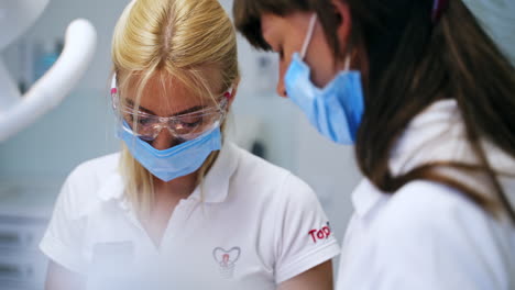 blonde female medic wearing protective goggles and mask looks down at the patient. dentist working in clinics.