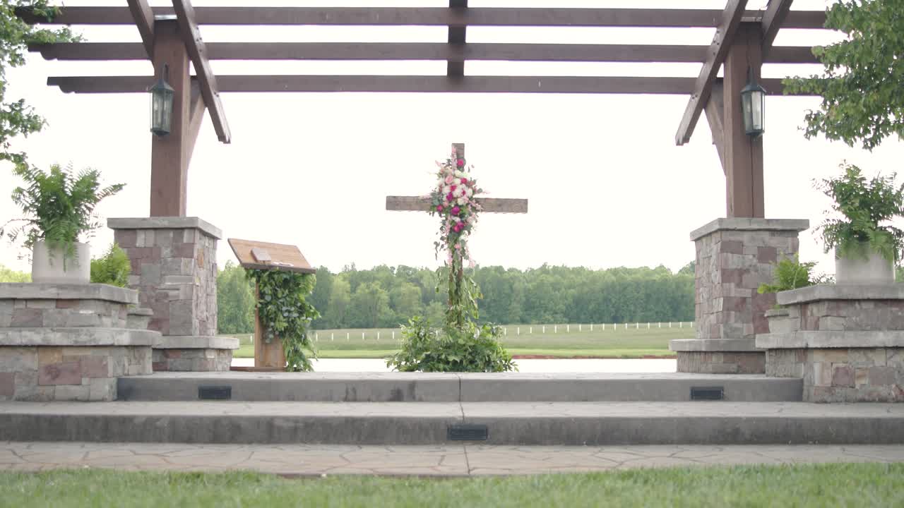 beautiful wedding cross altar with pink and white flowers and greenery with a lake behind
