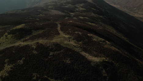 Hiker-alone-on-mountainside-with-reveal-of-misty-mountain-in-shadow-and-valleys-at-English-Lake-District-UK