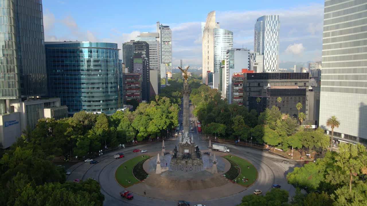 Establishing aerial view of Mexico City CDMX at the Angel of Independence roundabout on Paseo de la Reforma, green trees on a sunny day with modern buildings in the background