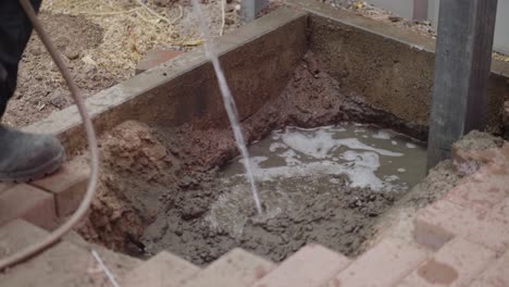 a construction worker adds water to cement in a hole, preparing the mixture for a building project. this footage captures the essential step of hydrating cement on a construction site.