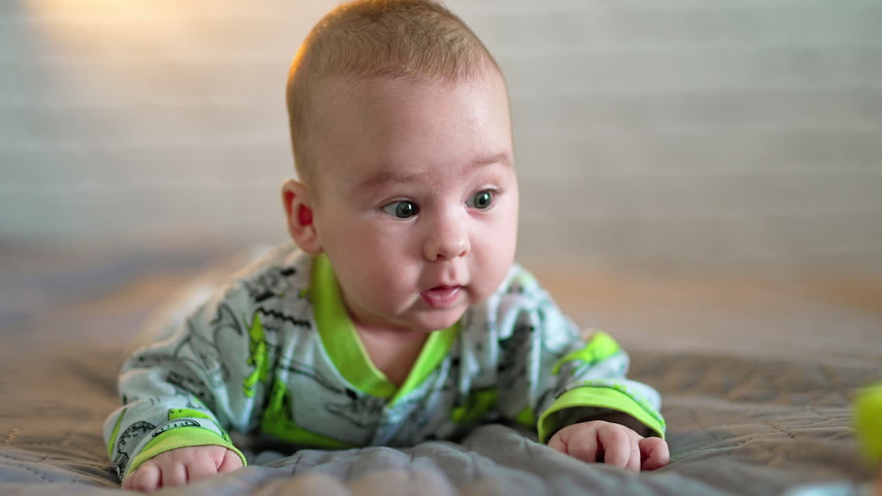 Funny infant baby lying on his belly and looking sideways. Close up portrait of a beautiful toddler boy. Grey backdrop.
