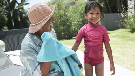 Biracial-woman-in-a-sunhat-smiles-at-a-biracial-girl-in-a-pink-swimsuit