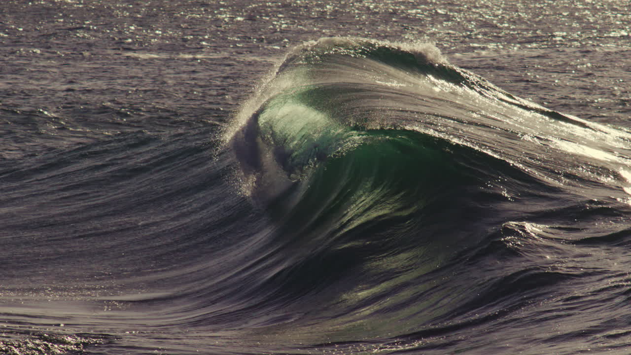 Shallow wave crest flows gently rightward, low golden light reflecting across water skin