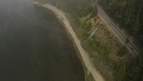 aerial tilt shot of traffic on a misty forest road on the coast of a sunny marsh