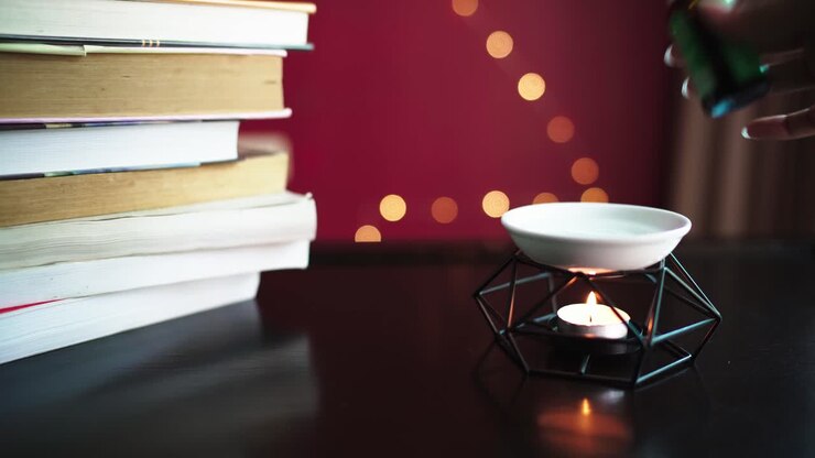 Primo piano di una lampada a olio con candela accesa su un tavolo e pila di libri a lato.