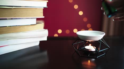 Close-up-oil-lamp-with-burning-candle-on-table-and-stack-of-books-on-side