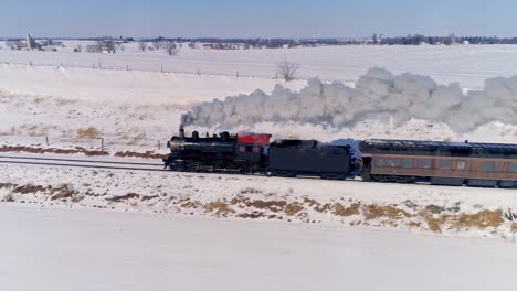 vista aérea de una antigua locomotora de vapor que se acerca tirando de automóviles de pasajeros y soplando humo y vapor después de una tormenta de nieve