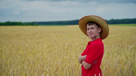 portrait of a little farmer on field. serious boy in straw hat standing on the golden field in summer day. agriculture and summer vacation.