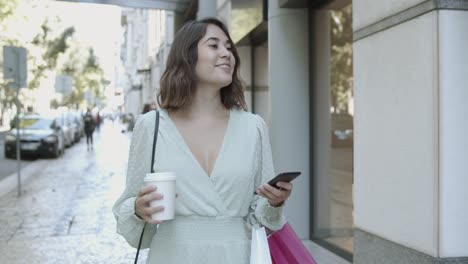 latin woman walking on street, drinking coffee and watching