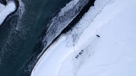 AERIAL:-Birdsview-of-Black-Beach-with-white-arctic-snow-in-Iceland-in-Winter-Snow,-Ice,-Waves,-Water