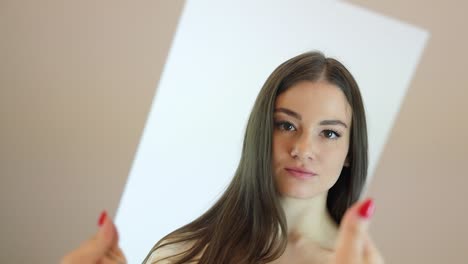 attractive caucasian girl lifting up a small mirror in front of her