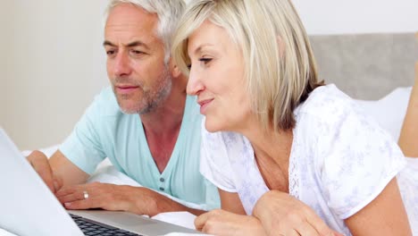 pareja feliz acostada en la cama usando una computadora portátil juntos