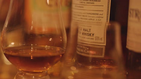 a whisky glass filled with amber spirit stands before several labeled bottles, illuminated by soft, warm lighting in a cozy indoor setting