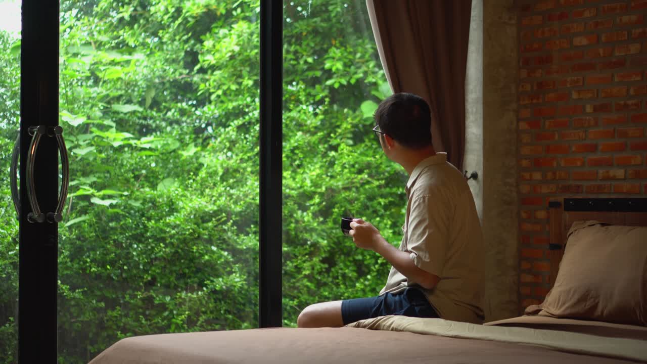 Handsome man resting and enjoying hot drink in bedroom. Relaxing holidays.