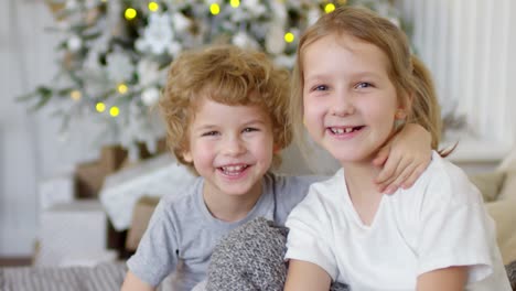 entzückender kleiner junge und seine süße schwester lächeln an weihnachten zu hause in die kamera