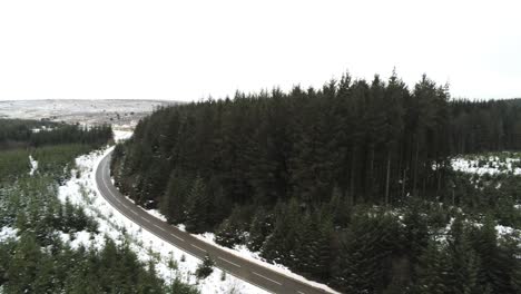 Snowy-Curved-Winter-Woodland-Road-Vista-Aérea-Hacia-Atrás-Siguiendo-El-Paisaje-De-árboles-Forestales