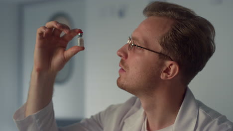 physician holding vaccine vial in hospital close up. man doctor examining fluid.