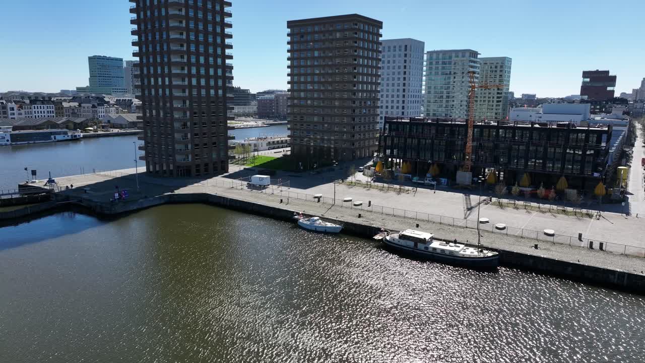 Semi orbit aerial view of Antwerp modern high-rise towers at the waterfront with boats docked and city background in daylight