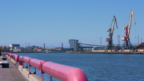 port cranes and harbor warehouses in sunny calm summer day at port of ventspils, venta river bank, wide shot from a distance