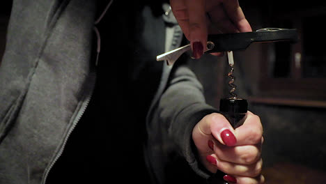 woman with red nail polish twisting bottle opener in a wine bottle cork